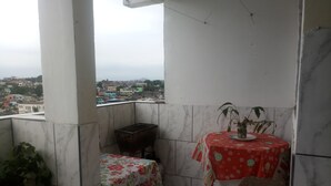 En balkon med et bord, stole, en plantekasse og udsigt over bybilledet.