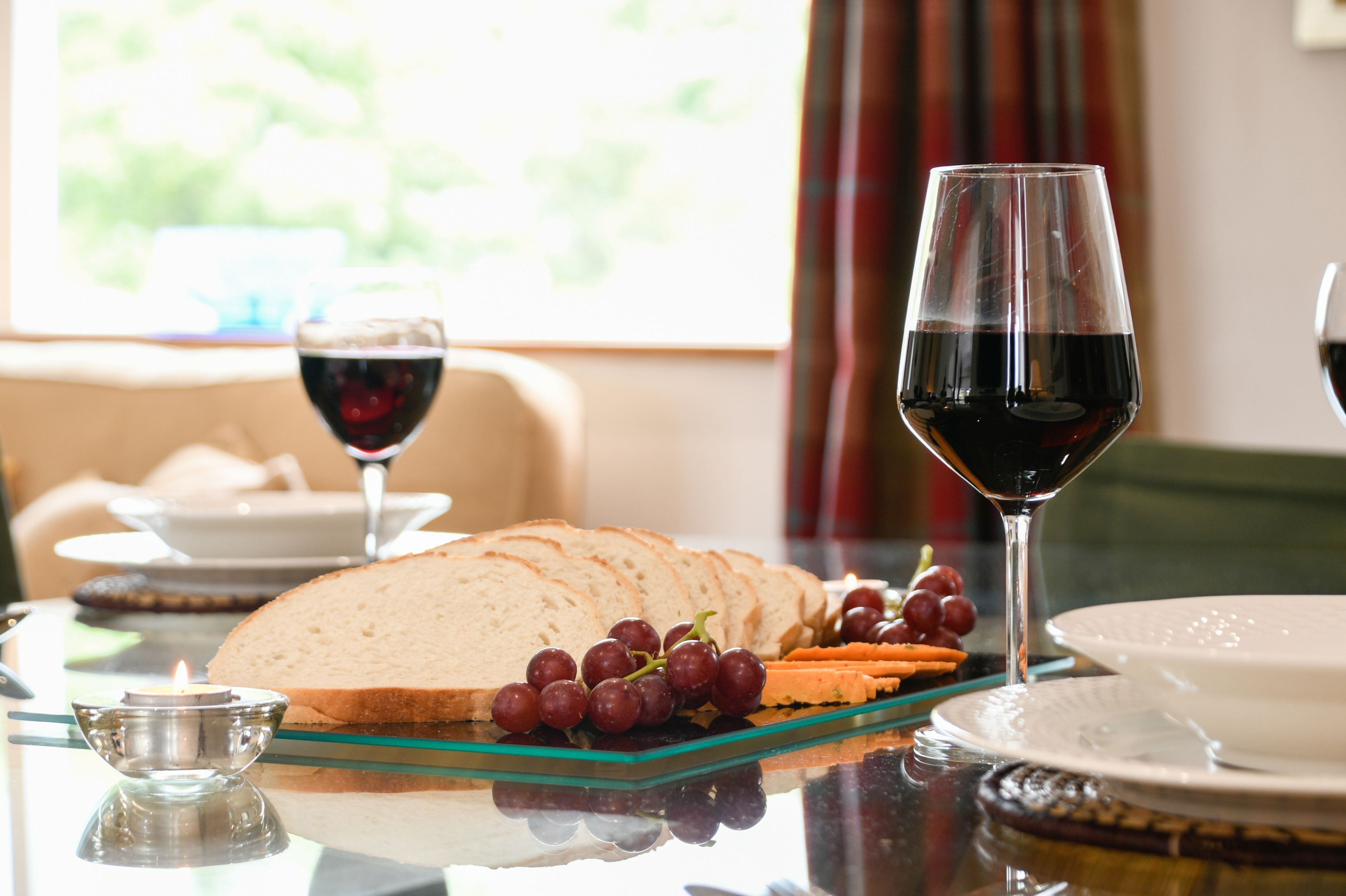 A dining table with a loaf of bread, a glass of red wine, and a plate of grapes.