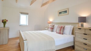 A bedroom with a bed, bedside tables, a dresser, a window, and a painting on the wall. - Peaceful Island Cottage (Oban)