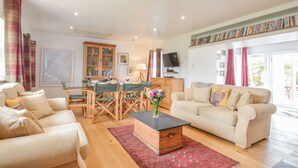A living room with a sofa, a coffee table, a dining table with chairs, a bookshelf, and a television. - Peaceful Island Cottage (Oban)
