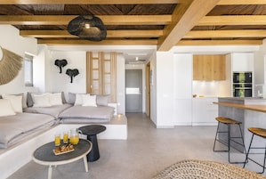 Una sala de estar moderna con un sofá, una mesa de centro con comida para el desayuno y una cocina con taburetes de bar.