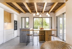 Una cocina moderna con una isla central, taburetes de bar y grandes ventanales que ofrecen vistas al verdor.