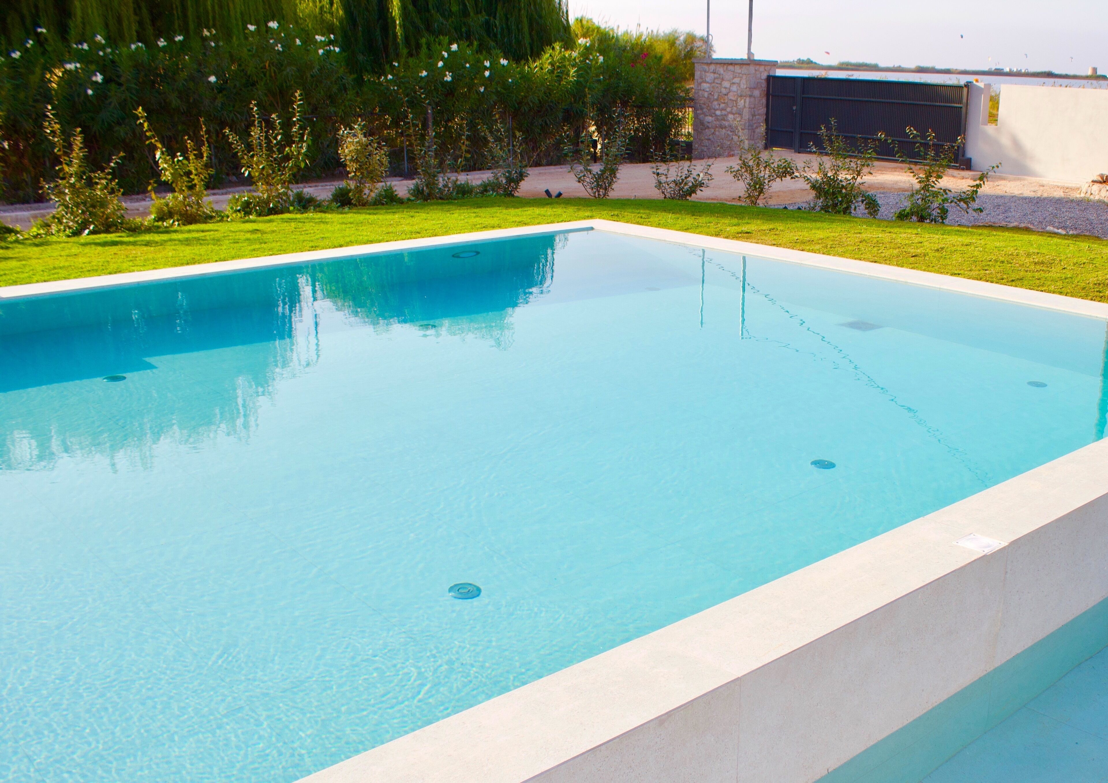 Una piscina rectangular con superficie de agua azul cristalina, rodeada por un césped bien cuidado y un muro de piedra.