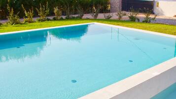Una piscina rectangular con superficie de agua azul cristalina, rodeada por un césped bien cuidado y un muro de piedra.