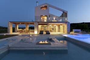A modern two-story house with a swimming pool, outdoor seating, and a fire feature. - Allure Retreat Villa (Lefkada)