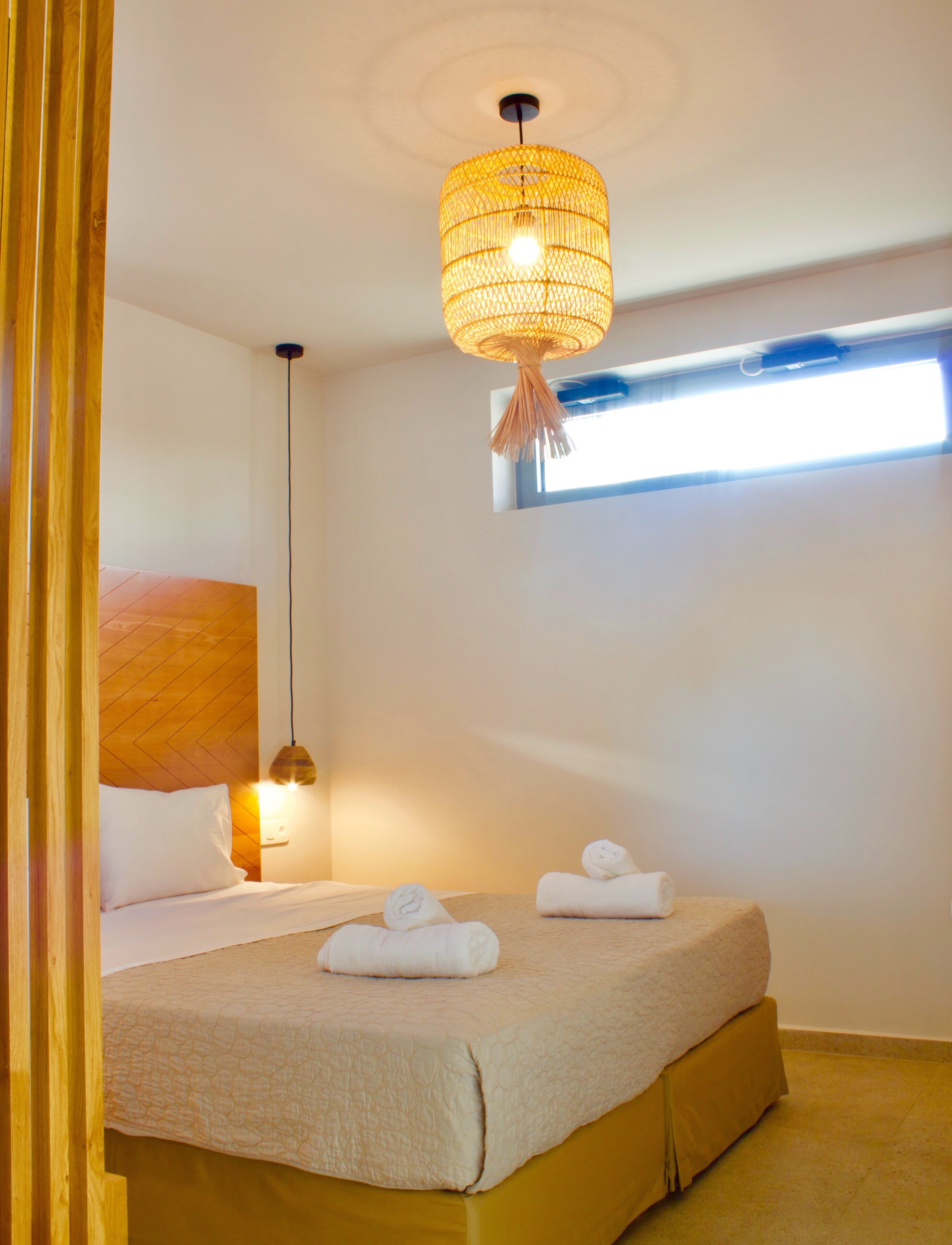 A bedroom with a bed, two towels, a hanging light fixture, and a window.