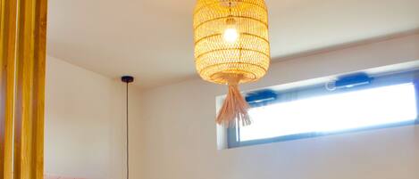 A bedroom with a bed, two towels, a hanging light fixture, and a window.