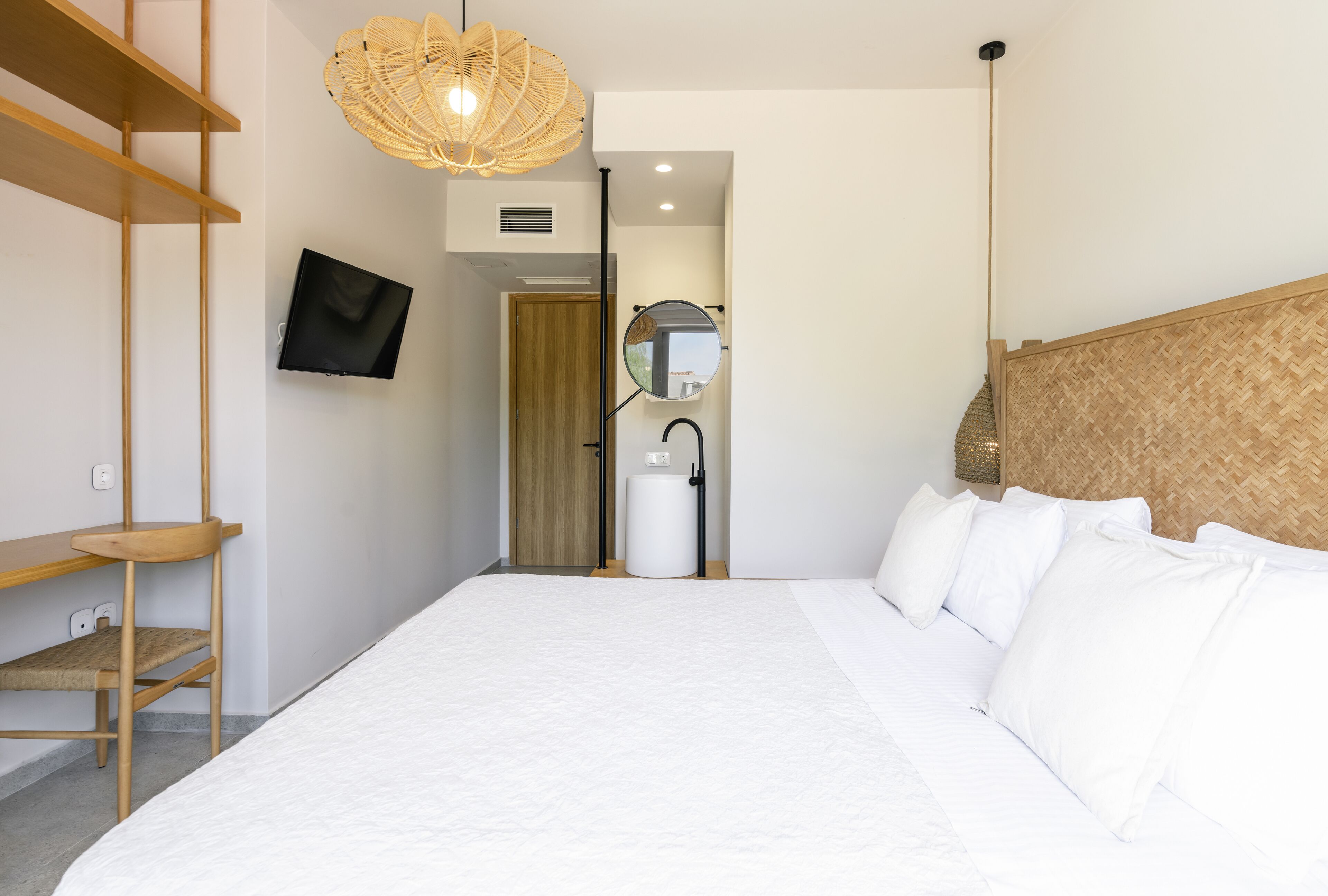 Une chambre d’hôtel moderne avec un grand lit, un téléviseur fixé au mur, une étagère en bois, une lampe en osier et un miroir.