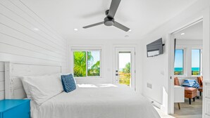 Een slaapkamer met een bed, een plafondventilator, een aan de muur bevestigde televisie en uitzicht op de omgeving door een raam.