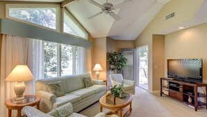 A spacious living room with a sofa, armchairs, a coffee table, a television, and a ceiling fan. - Brigantine Quarters, Shipyard Plantation, Hilton Head 2 bed/2 bath condo (Hilton Head)