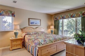 Une chambre à coucher avec un lit, deux tables de chevet, une fenêtre avec des rideaux et un tableau encadré au mur.