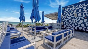 Un salon sur le toit, doté de sièges bleus rembourrés, de parasols et d’un mur orné de motifs.