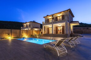 A two-story stone house with a swimming pool and outdoor seating.