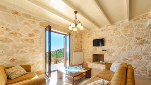 A spacious living room with stone walls, a large sofa set, a coffee table, and a TV mounted on the wall. - Orient Villas Deluxe (Zakynthos)