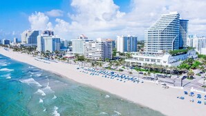 Um hotel na praia com vários edifícios altos, uma praia de areia e muitos guarda-sóis azuis.