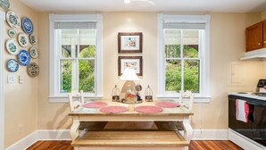 A kitchen with a wooden table, two windows, and a stove. - Enchanting Cottage, walk to Downtown Harpers Ferry (Harpers Ferry)
