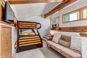Un lit superposé avec un téléviseur à gauche, un canapé avec des coussins à motifs et une fenêtre avec des rideaux à droite.