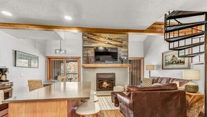 A spacious living area with a fireplace, a wooden ceiling, and a stone wall. - New Listing! Perfectly Located Breckenridge Condo, Ski Off, Walk to Town! (Breckenridge)