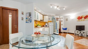 A modern kitchen with white cabinets, a microwave, and a refrigerator. There is a dining area with a glass table and white chairs. - Casa Querida Central and Elegant Flat (Naples)
