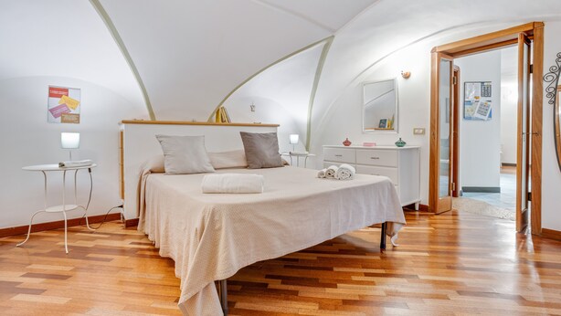 A bedroom with a bed, a bedside table, a nightstand, and a wooden floor. - Casa Querida Central and Elegant Flat (Naples)