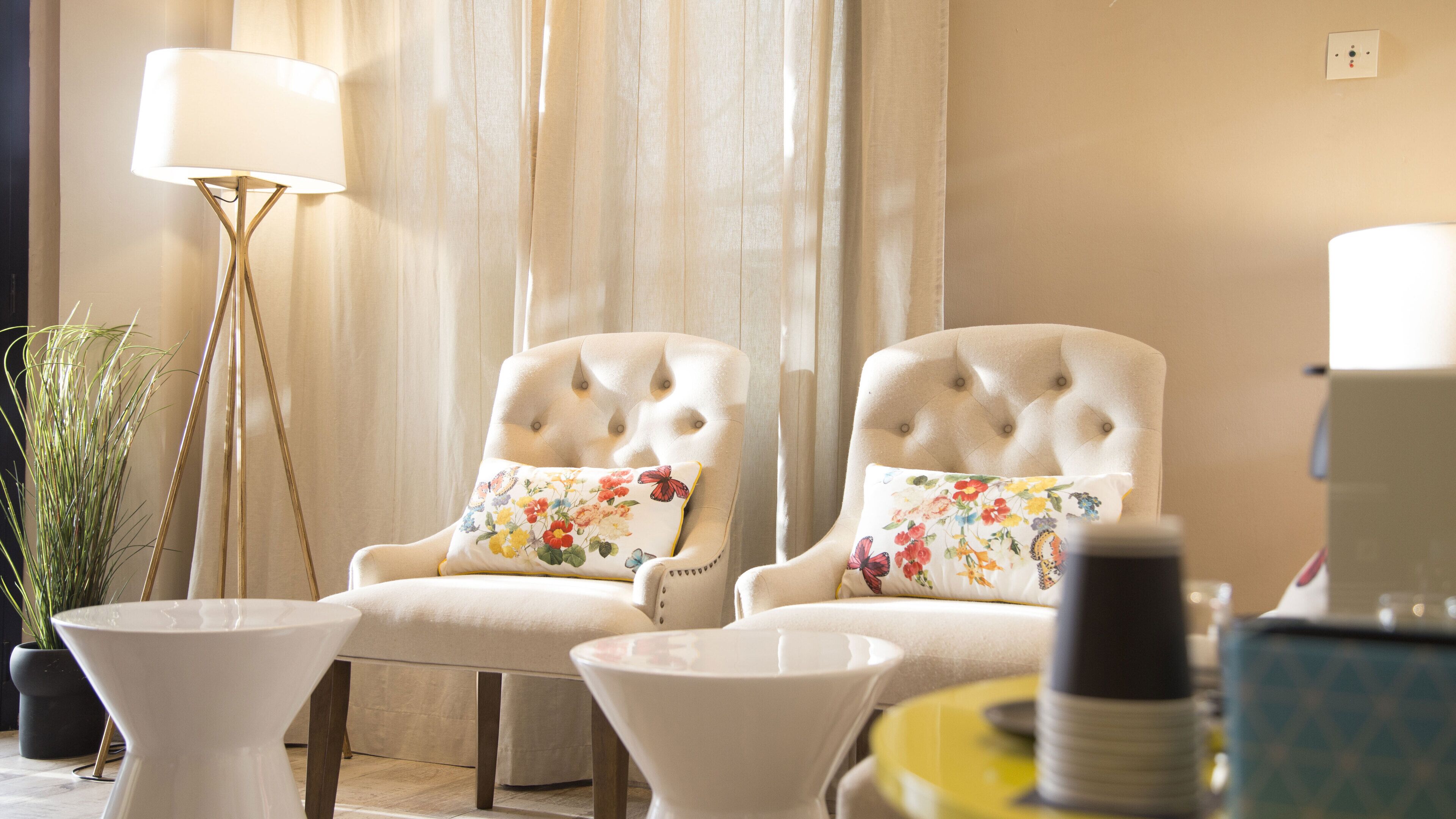 A room with two tufted armchairs with floral cushions, a floor lamp, and a small white table.