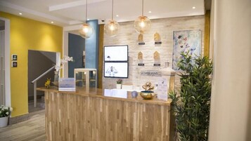 Un área de recepción con un mostrador de madera, lámparas colgantes, un televisor montado en la pared y una planta.
