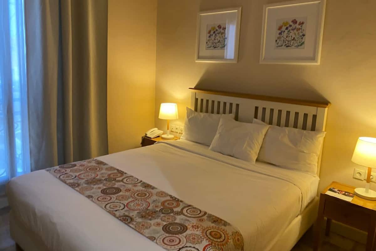 Quarto de hotel com uma cama, duas luminárias de cabeceira, um telefone e duas obras de arte emolduradas na parede.