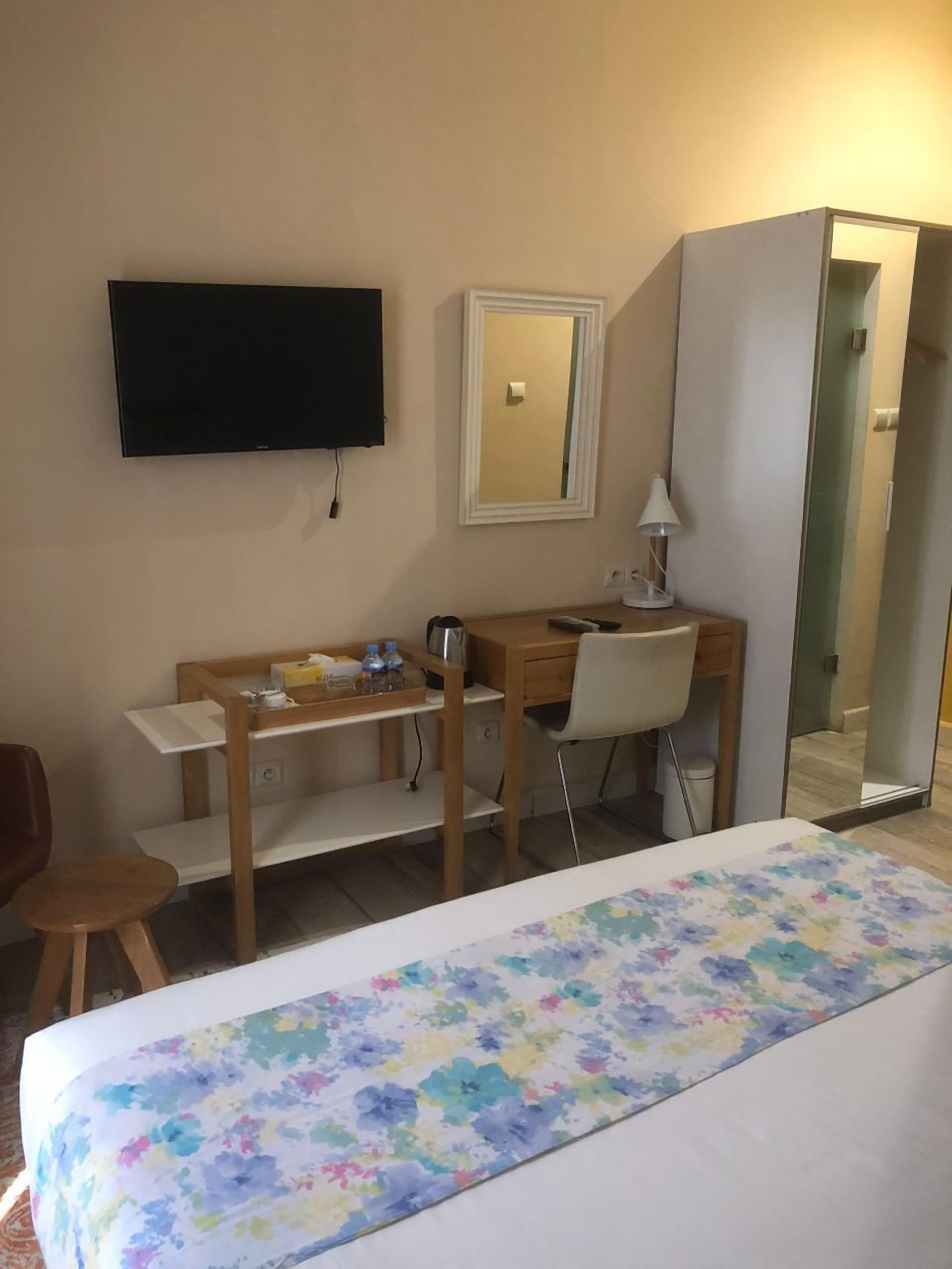A hotel room with a bed, a desk with a chair, a television, a mirror, and a wardrobe.