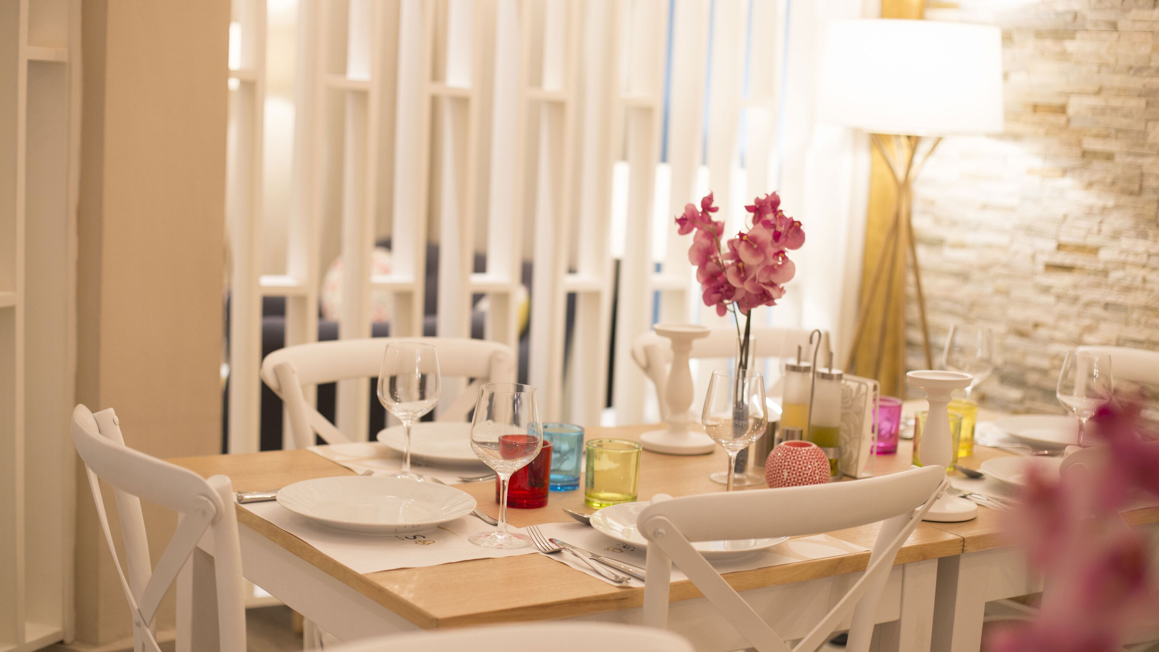 A dining area with white chairs, a wooden table, and a vase of pink flowers.
