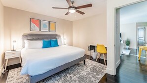 Un dormitorio moderno con una cama grande, un ventilador de techo y vistas al área de estar contigua.