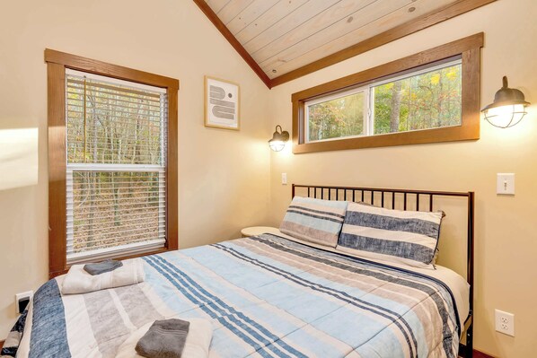 Un dormitorio con una cama, dos ventanas y un techo con vigas de madera.