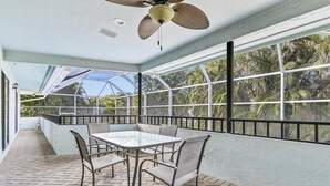 Eine überdachte Terrasse mit Tisch und Stühlen, großen Fenstern und einem Deckenventilator.
