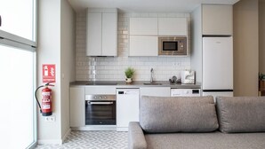 A modern kitchen with white cabinets, a microwave, a refrigerator, and a dishwasher. There is a fire extinguisher mounted on the wall and a small plant on the counter. - Port Suite X | 4 Guests  | AC & WiFi | 15 min Ciudad Artes (Valencia)