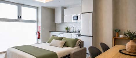 A modern bedroom with a bed, bedside table, and a view of a kitchenette.