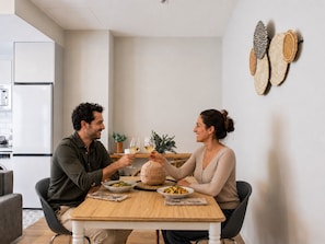 A modern kitchen with a dining table, two people toasting with wine glasses, and a small plant on the counter. - Port Suite X | 4 Guests  | AC & WiFi | 15 min Ciudad Artes (Valencia)