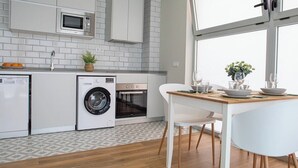 A modern kitchen with built-in appliances, a dining area with a table and chairs, and a large window providing natural light. - Port Suite V | 4 Guests | AC & WiFi | 15 min Ciudad Artes (Valencia)