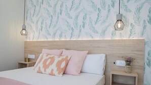 A neatly arranged bedroom with a wooden headboard, a bed with pink and white bedding, two bedside tables with lamps, and a wall with a leaf pattern. - Port Suite V | 4 Guests | AC & WiFi | 15 min Ciudad Artes (Valencia)