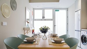 A dining area with a wooden table set for four, surrounded by green chairs. A vase with flowers is placed in the center. - Port Suite III | 6 Guests | AC & WiFi | 15 min Ciudad Artes (Valencia)