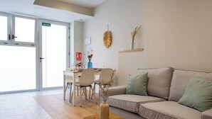 A modern living room with a sofa, a coffee table, and a dining area with chairs and a table. - Port Suite II | 4 Guests | AC & WiFi | 15 min Ciudad Artes (Valencia)