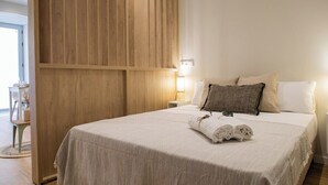 A neatly made bed with a white bedspread and two pillows, a wooden panel wall, and a small bedside table with a lamp. - Port Suite II | 4 Guests | AC & WiFi | 15 min Ciudad Artes (Valencia)