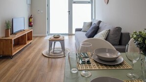 Een moderne woonkamer met een grijze bank, een houten tv-meubel en een eettafel gedekt met kommen en wijnglazen.