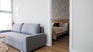 Una sala de estar moderna con un sofá gris, una pequeña mesa de madera y un dormitorio con papel tapiz estampado.