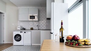 Una cocina moderna con lavadora, una botella de vino y fruta en la encimera.