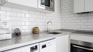 Una cocina moderna con armarios blancos, microondas integrado, lavavajillas y horno.