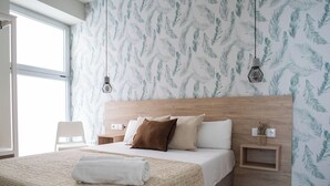 Un dormitorio moderno con una cama grande, cabecera de madera y papel tapiz con estampado de hojas. Hay dos mesitas de noche con lámparas y un pequeño estante con una planta.