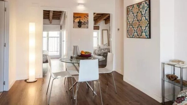 Un comedor moderno con una mesa de vidrio, sillas blancas y techo de madera.