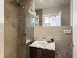 Ein modernes Badezimmer mit einer Duschkabine, einem weißen Waschbecken und einem Spiegel.