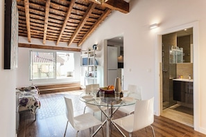 A modern interior with a glass dining table, white chairs, a wooden ceiling, and a kitchen area with a glass shower.