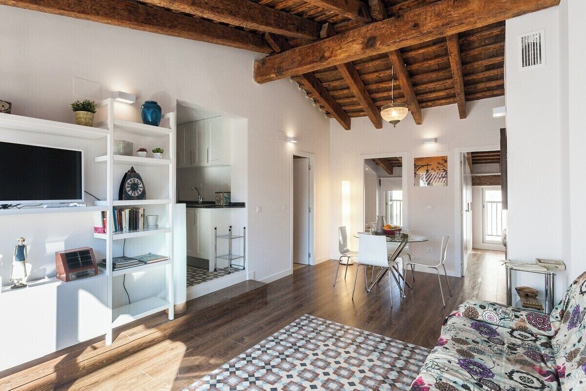 Een moderne woonkamer met een houten plafond, witte kasten, een kamerbreed tapijt en een eethoek met stoelen en een tafel.