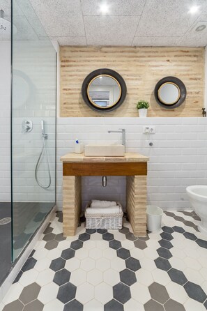 Une salle de bain moderne avec un meuble-lavabo en bois, deux miroirs ronds, une cabine de douche en verre et un sol carrelé avec des carreaux hexagonaux.